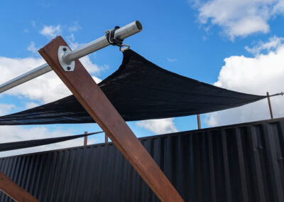 A detailed look at the shade structure's support mechanism, showcasing sturdy construction elements against a blue sky, adding charm to outdoor spaces in cabins, dwellings, caravans, & glamping tents.