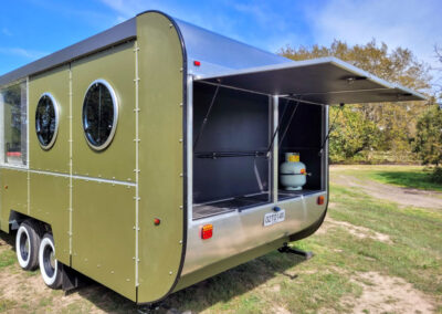 Back view of a modern green caravan with a pop-up hatch revealing a storage area equipped with a propane tank, ideal for Cabins, Dwellings, Caravans, & Glamping Tents. This versatile design offers convenient storage and outdoor utility, perfect for adventurers seeking a well-equipped and stylish mobile accommodation