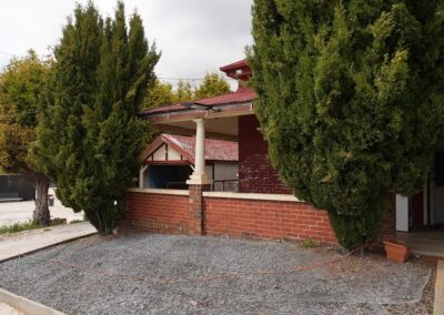 Charming red-brick exterior of a rustic dwelling surrounded by tall, lush trees, featuring a covered porch with columns, ideal for Cabins, Dwellings, Caravans, & Glamping Tents. The outdoor area provides a natural, peaceful setting, perfect for guests seeking a cozy retreat in a rural environment