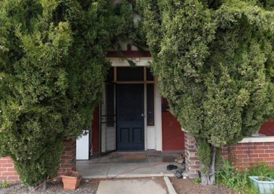 Charming entrance to a rustic dwelling framed by lush greenery and red brick walls, ideal for visitors to Cabins, Dwellings, Caravans, & Glamping Tents. The shaded doorway provides a welcoming feel, enhancing the natural, cozy appeal of the accommodation surrounded by nature