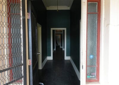 View through an open front door leading into a long hallway with dark walls and high ceilings, ideal for Cabins, Dwellings, Caravans, & Glamping Tents. This inviting entryway, framed by secure mesh door and glass panels, provides a welcoming glimpse into the rustic interior, perfect for guests seeking a cozy and secure retreat