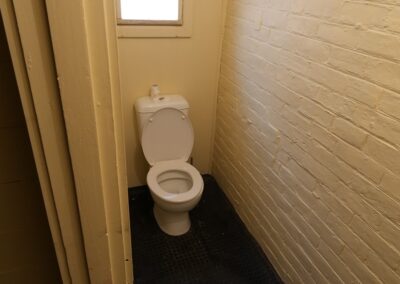 Simple and clean restroom with a white toilet, featuring painted brick walls and a small window, suitable for guests in Cabins, Dwellings, Caravans, & Glamping Tents. This minimalist bathroom setup provides essential facilities for a comfortable stay in rustic or glamping accommodations