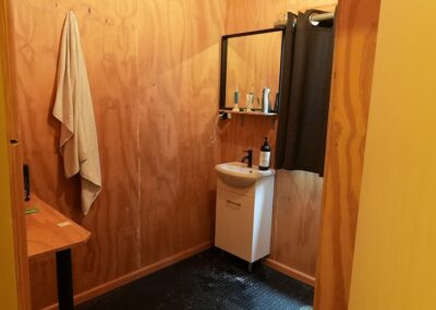 Rustic bathroom with wooden walls, a small sink, mirror, and essential toiletries, ideal for guests in Cabins, Dwellings, Caravans, & Glamping Tents. The natural wood paneling and minimalistic design create a warm, inviting atmosphere, perfect for travelers seeking a cozy and functional bathroom setup