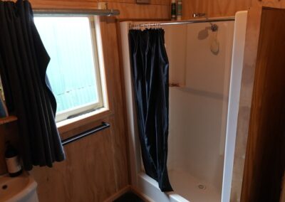 Rustic bathroom with a standalone shower featuring a dark curtain, wooden walls, and natural lighting, ideal for guests in Cabins, Dwellings, Caravans, & Glamping Tents. This cozy shower area combines functional amenities with a warm, natural ambiance, perfect for travelers seeking comfort in a rural setting