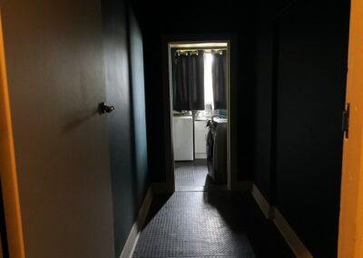 Dimly lit hallway leading to a laundry room with a washing machine and dryer, ideal for guest use in Cabins, Dwellings, Caravans, & Glamping Tents. This functional space offers convenient amenities for travelers looking for self-service laundry facilities during their stay