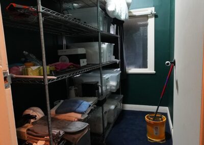 A well-organized storage room with metal shelving units holding various supplies, including towels, containers, and cleaning products, ideal for maintaining Cabins, Dwellings, Caravans, & Glamping Tents. A mop bucket stands ready in the corner, showcasing essential maintenance and cleaning setup for comfortable guest accommodations